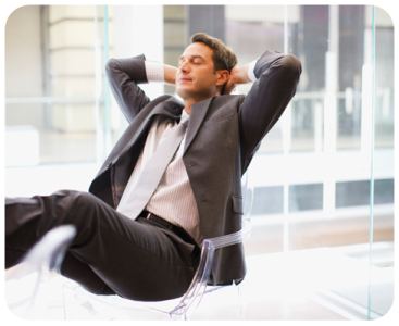 A man in suit and tie sitting on chair with hands behind head.